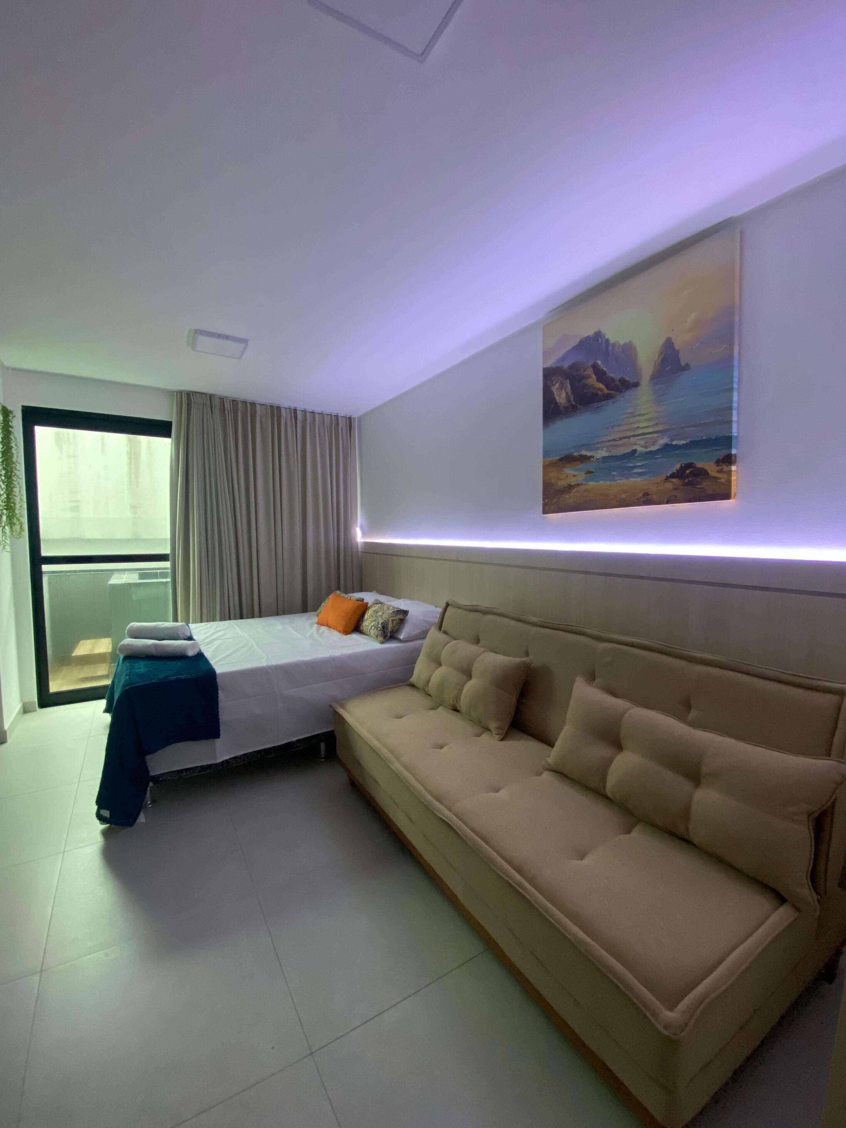 A modern hotel room with a bed, a sofa, a painting, and a large window.