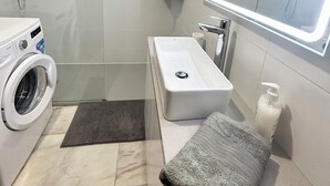 A modern bathroom with a washing machine, a sink, a shower, and a large mirror.