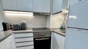 A modern kitchen with white cabinets, a stainless steel range hood, a built-in oven, and a refrigerator.