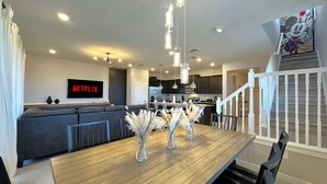 Una sala de estar moderna con una mesa de comedor de madera, sofá gris y una cocina al fondo.