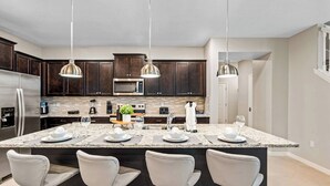 Una cocina moderna con gabinetes de madera oscura, electrodomésticos de acero inoxidable y una isla de granito con asientos tipo barra.