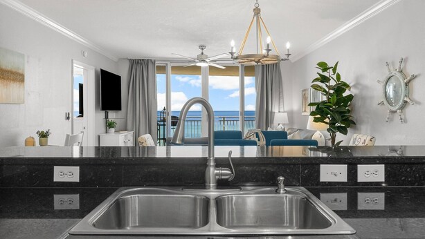 A modern kitchen with a double sink, a chandelier, and a view of the ocean. - Gulf-Front 2 Bed, 2 Bath • Sleeps 8 • Amenity-Packed • Beach Chair Service for 2 (Panama City Beach)