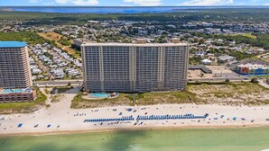 A high-rise hotel with multiple floors, a pool, and a beach area with umbrellas. - Gulf-Front 2 Bed, 2 Bath • Sleeps 8 • Amenity-Packed • Beach Chair Service for 2 (Panama City Beach)