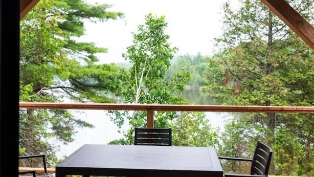 A wooden deck with a table and chairs, overlooking a lake and trees. - Waterfront lux loft 2 bedroom perfect for couples (Pontiac)