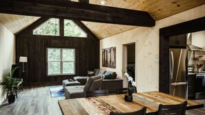 A spacious loft with a high ceiling, wooden beams, a large dining table, and a cozy seating area with a sofa and chairs. - Waterfront lux loft 2 bedroom perfect for couples (Pontiac)