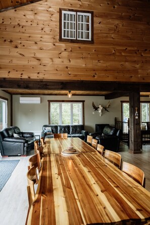 Une pièce spacieuse avec une grande table à manger en bois, entourée de chaises, d’un canapé en cuir et d’un plafond en bois avec des poutres apparentes.
