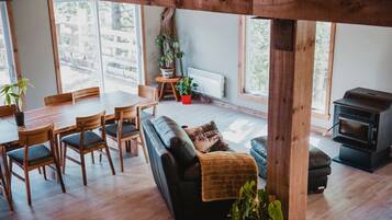 Una sala de estar acogedora con una mesa de comedor de madera, un sofá negro y un estufa de leña.
