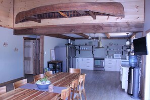 Une cuisine spacieuse avec des poutres en bois, un coin repas avec une table et des chaises en bois, et un grand distributeur d’eau.