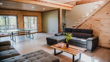 Amplia sala de estar con techo de madera, una escalera, sofá, mesa de centro y vistas al exterior.