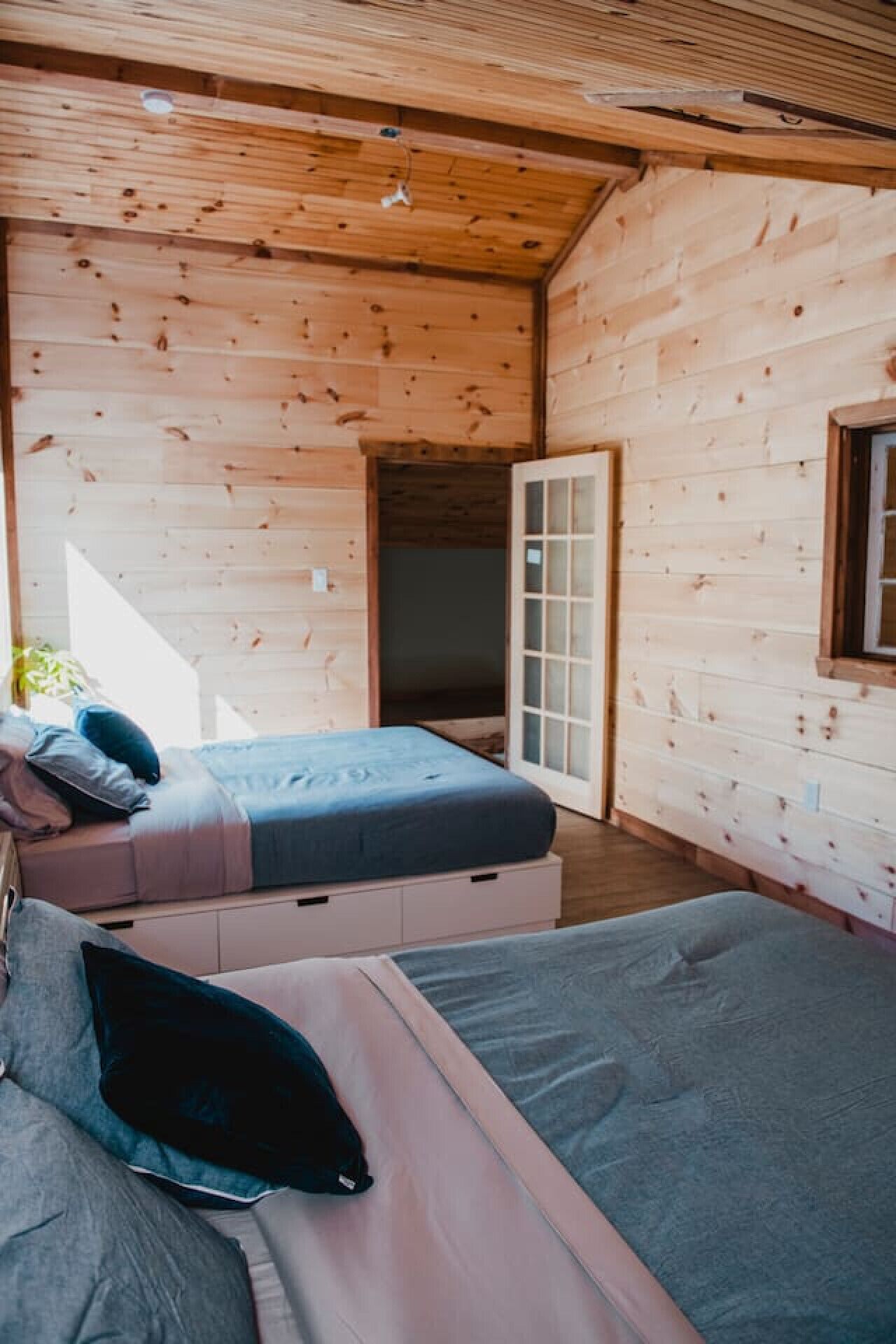 A wooden cabin room with a bed, a sofa, and a window.