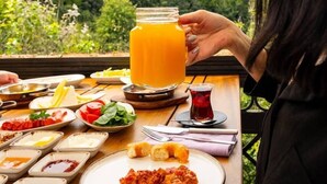 A dining table with various dishes and a large glass of orange juice, set against a backdrop of a lush green landscape. - Villa Polonez (Beykoz)
