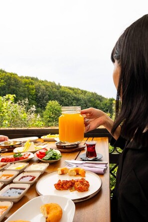 Ein Esstisch mit verschiedenen Gerichten und einem großen Glas Orangensaft, vor einer üppigen, grünen Landschaft.