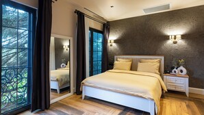 Une chambre à coucher avec un grand lit, une table de chevet, un miroir et une vue sur les arbres par la fenêtre.