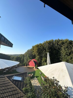 A covered outdoor area with a stage, seating, and a view of a forested hillside. - Villa Polonez (Beykoz)