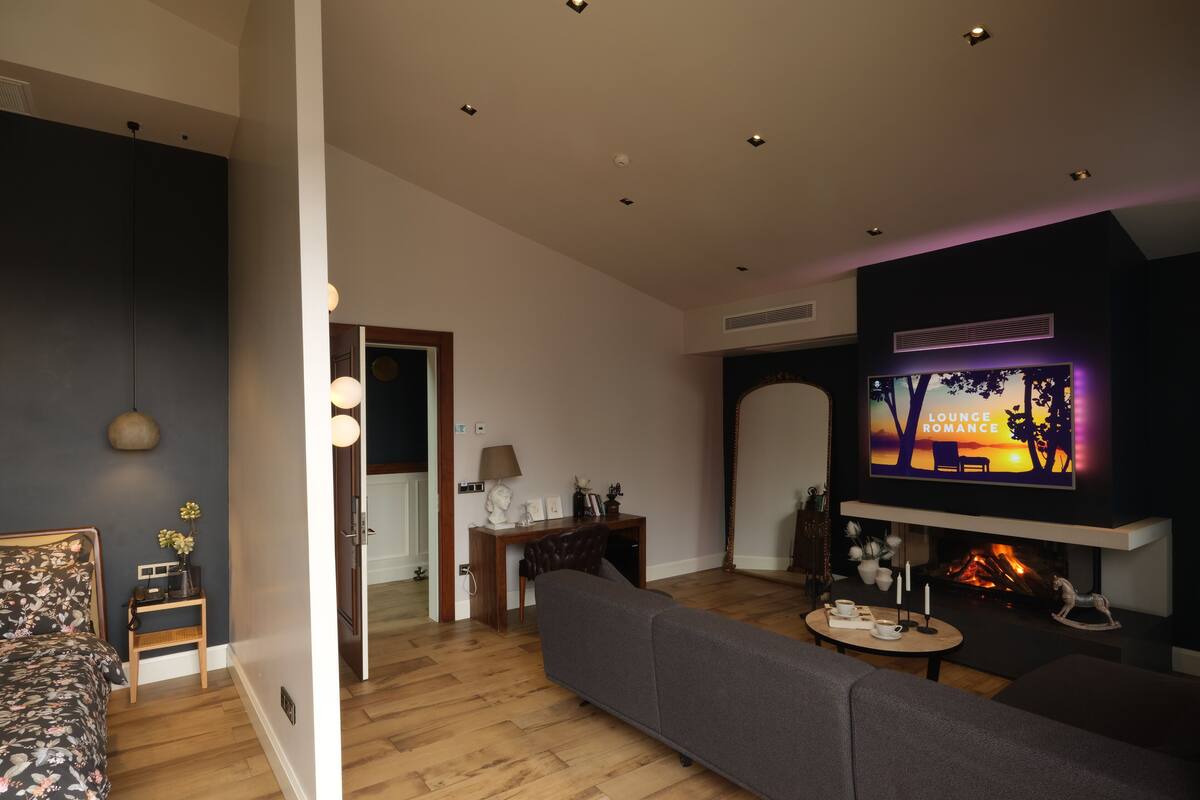 A modern living room with a sofa, a TV displaying 'LOUNGE ROMANCE', a fireplace, and a wooden floor.