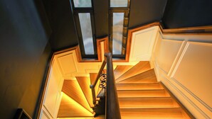 Un escalier avec des marches en bois et des murs blancs, menant à un palier doté d’une fenêtre.