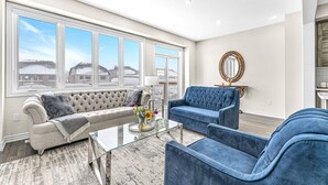 Ein geräumiges Wohnzimmer mit großem Fenster, einer Couch, einem Zweisitzer und einem Glastisch.