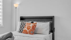 A bed with a dark headboard, white bedding, and a single orange and gray patterned pillow. - Beautiful New Build by Elora (Fergus)