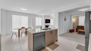 A modern kitchen with a dishwasher, a dining area with a table and chairs, a TV mounted on the wall, and a living area with a sofa and a patterned wall. - Beautiful New Build by Elora (Fergus)