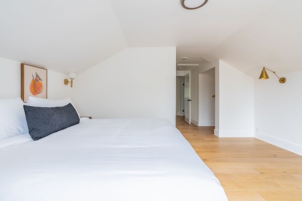 A bedroom with a large bed, a framed picture on the wall, and a hallway leading to another room.