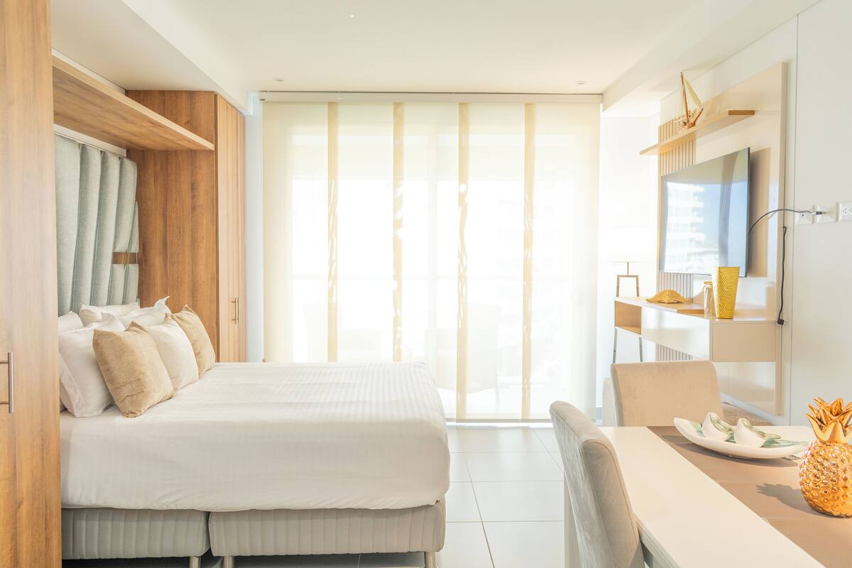A hotel room with a bed, a dining table with a pineapple, and a TV on the wall.
