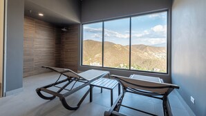 Una habitación moderna con un ventanal grande, dos sillones reclinables y una mesita pequeña.