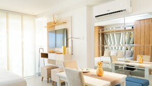 Habitación de hotel moderna con una cama grande, un área de comedor con mesa y sillas, un televisor y un ventanal amplio.