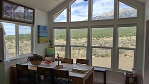 Ein Essbereich mit Tisch, Stühlen und Blick auf eine Wüstenlandschaft durch große Fenster.