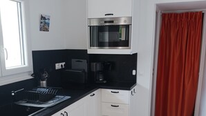 Een kleine keuken met witte kastjes, een zwart aanrecht, een oven van roestvrij staal en een koffiezetapparaat.