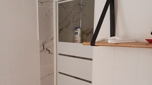 Een badkamer met een douche, witte betegelde wanden, een marmerlook spatwand en een handdoekrek met een handdoek.