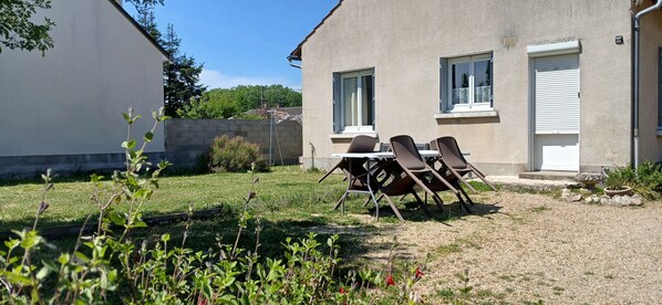 A patio with a table and chairs, a gravel area, and a building with windows and a door.
