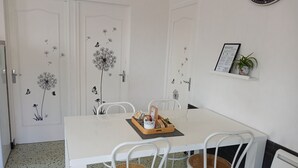 Un comedor con una mesa blanca, dos sillas de mimbre y un reloj en la pared.