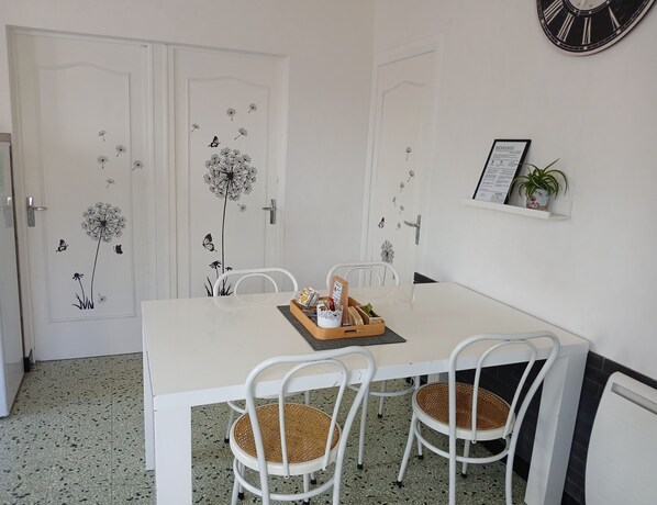 A dining area with a white table, two wicker chairs, and a clock on the wall.