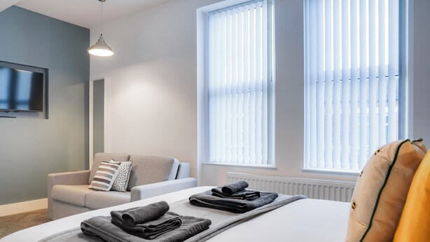 A modern hotel room with a neatly made bed, a sofa, and a television on the wall.