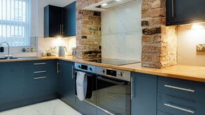 A modern kitchen with dark cabinets, a brick accent wall, a marble backsplash, and stainless steel appliances.