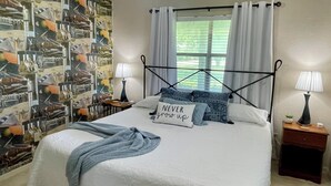 A bedroom with a bed, two bedside tables, a window with curtains, and a wall with a patterned mural.