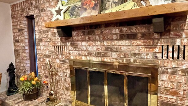A brick fireplace with a star decoration, a shelf with framed pictures, and a vase with flowers.