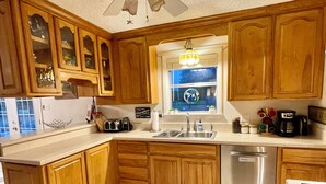 A kitchen with wooden cabinets, a stainless steel dishwasher, and a window with a view of the outdoors.