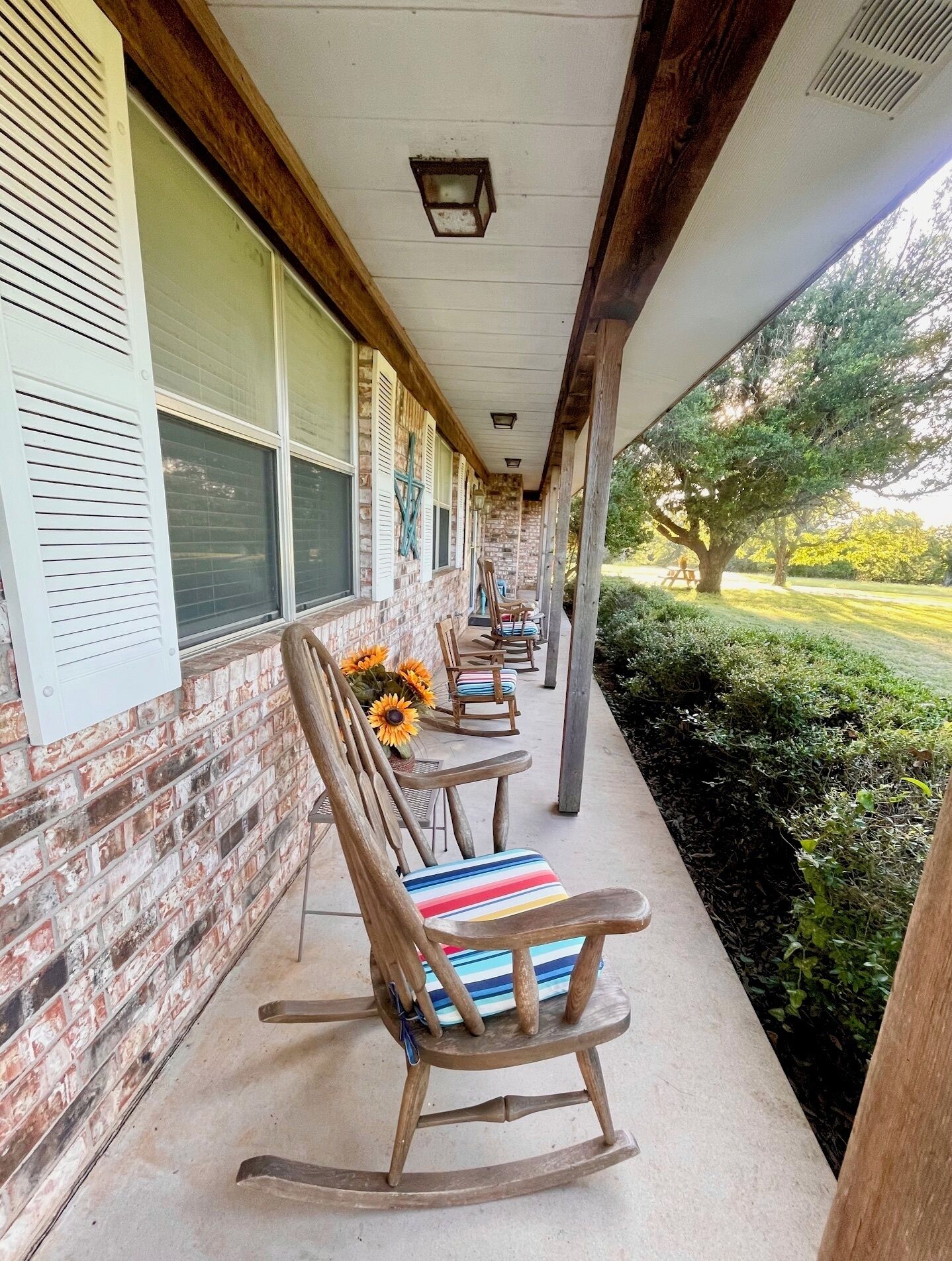 A covered porch with rocking chairs and a brick wall.