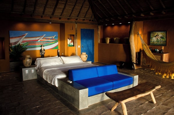 A bedroom with a bed, a blue sofa, a wooden bench, a hammock, and a painting of a boat on the wall. - Cala Margarita Hotel Boutique & Spa (ParaguachÃ)