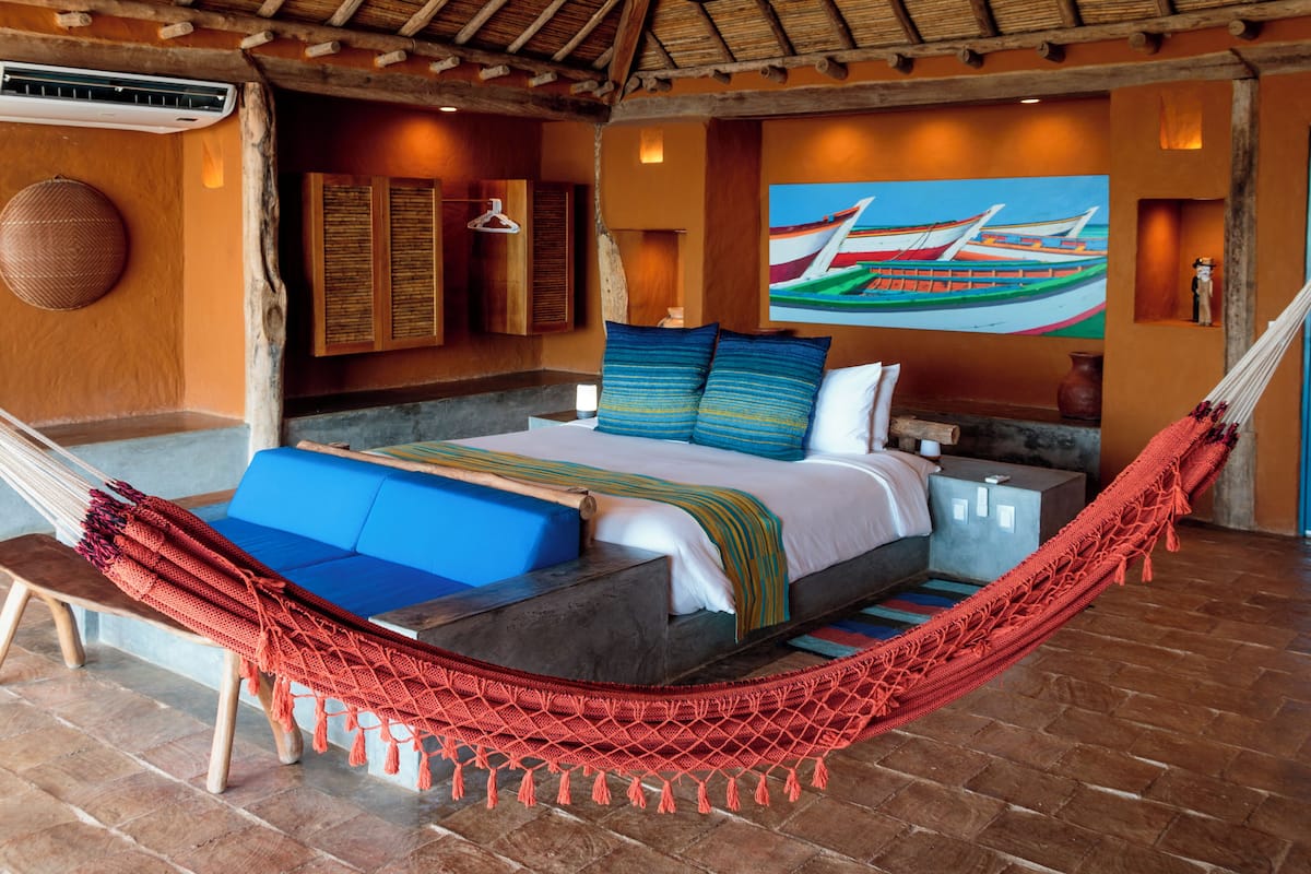 Una habitación con una cama, una hamaca, un sofá azul y un cuadro de barcos en la pared.