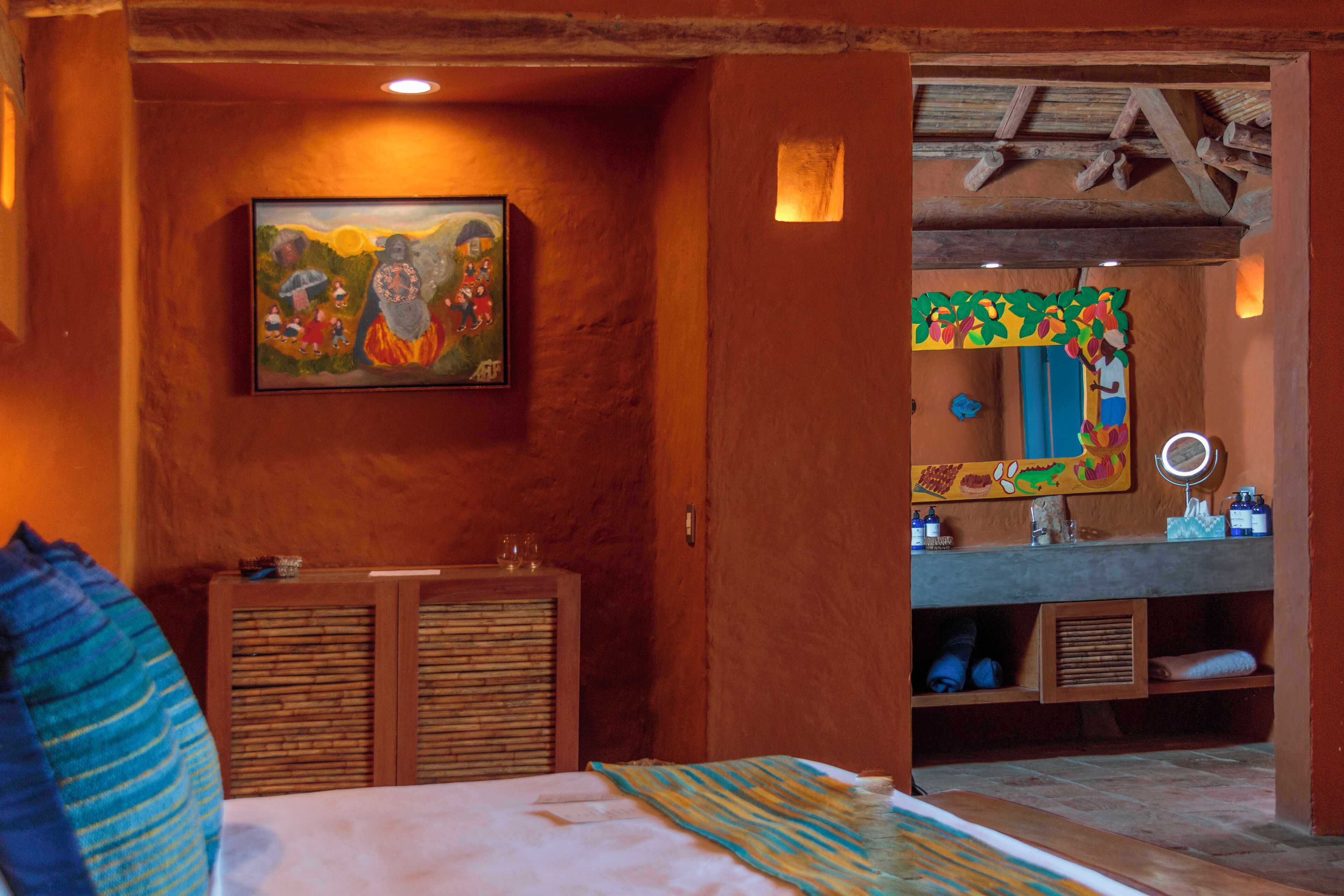 Een kamer met een bed, een schilderij aan de muur, een badkamer met een spiegel en houten kastjes.