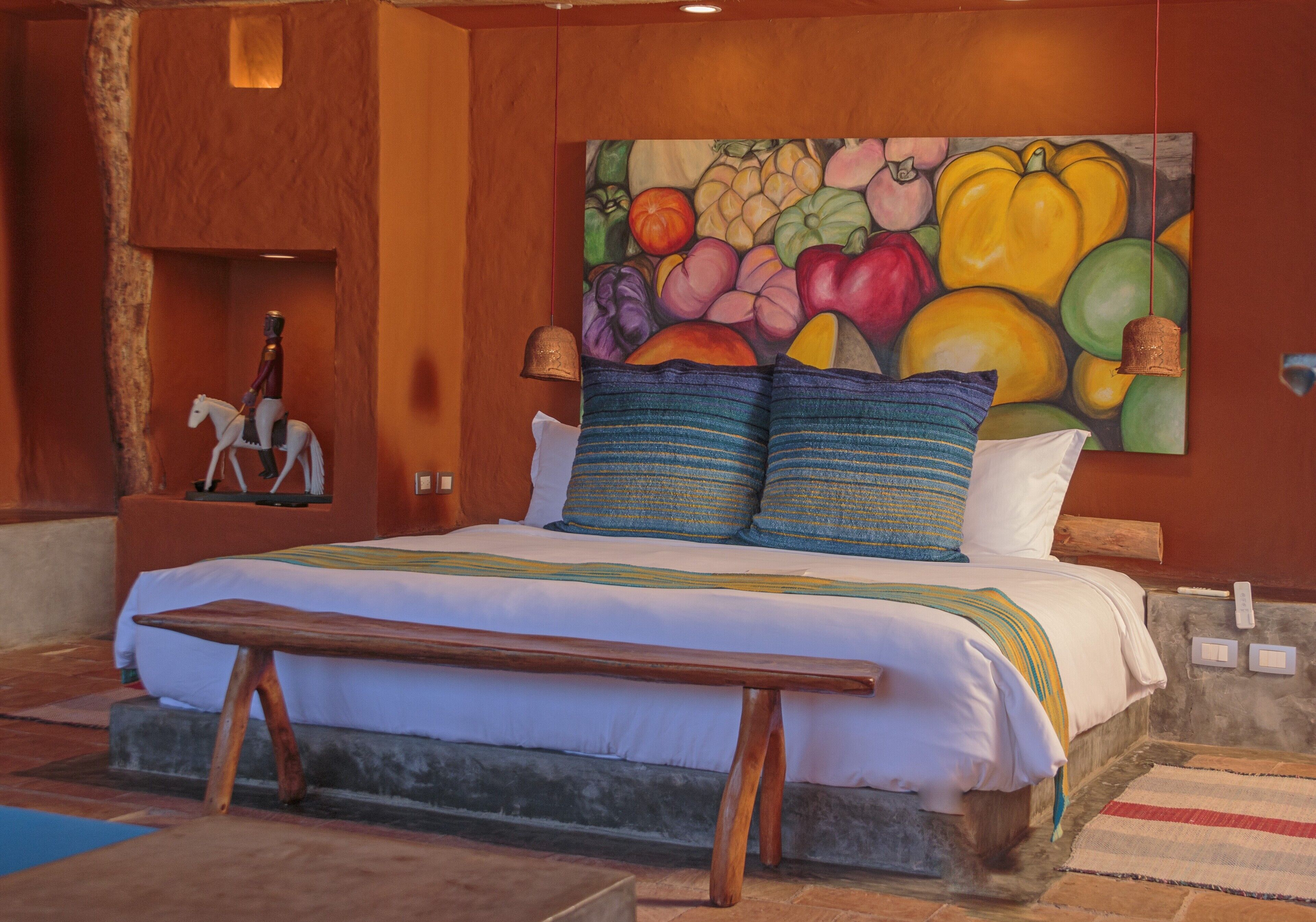 A bedroom with a bed, pillows, a bench, a painting, and a bell.