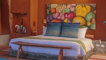 A bedroom with a bed, pillows, a bench, a painting, and a bell.