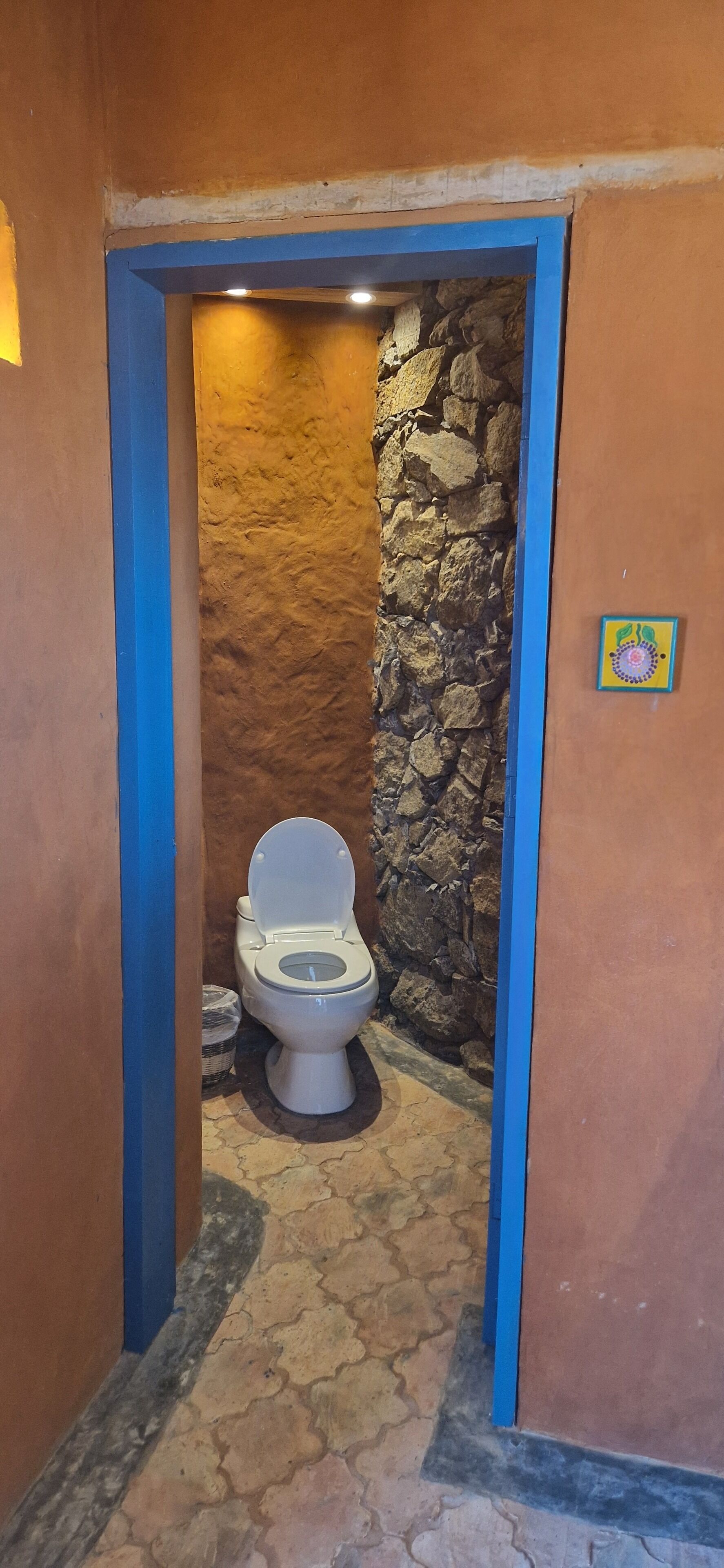 A narrow bathroom with a stone wall, a white toilet, and a blue door frame.