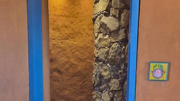 A narrow bathroom with a stone wall, a white toilet, and a blue door frame.