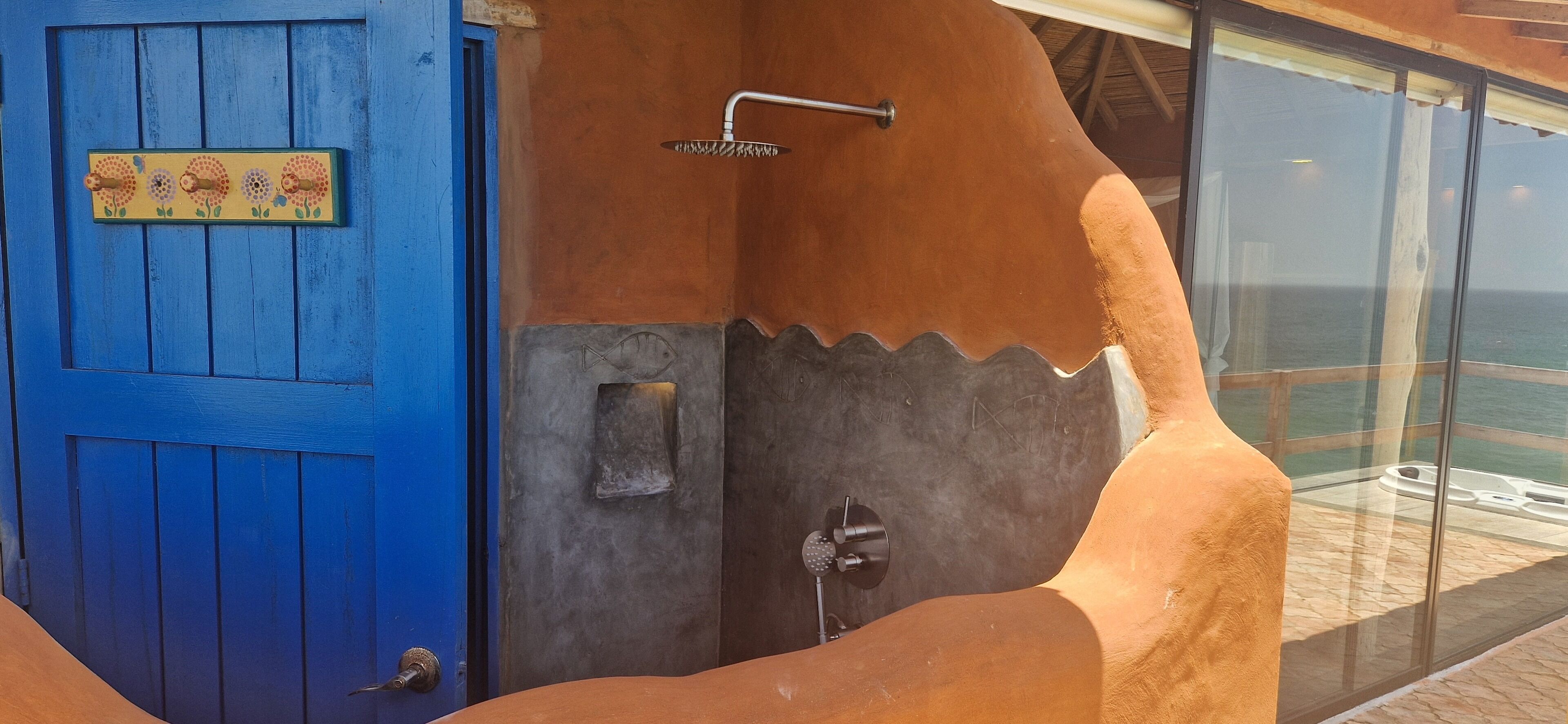 Una puerta azul con una placa decorativa, un área de ducha con ducha y vistas al océano a través de amplios ventanales.