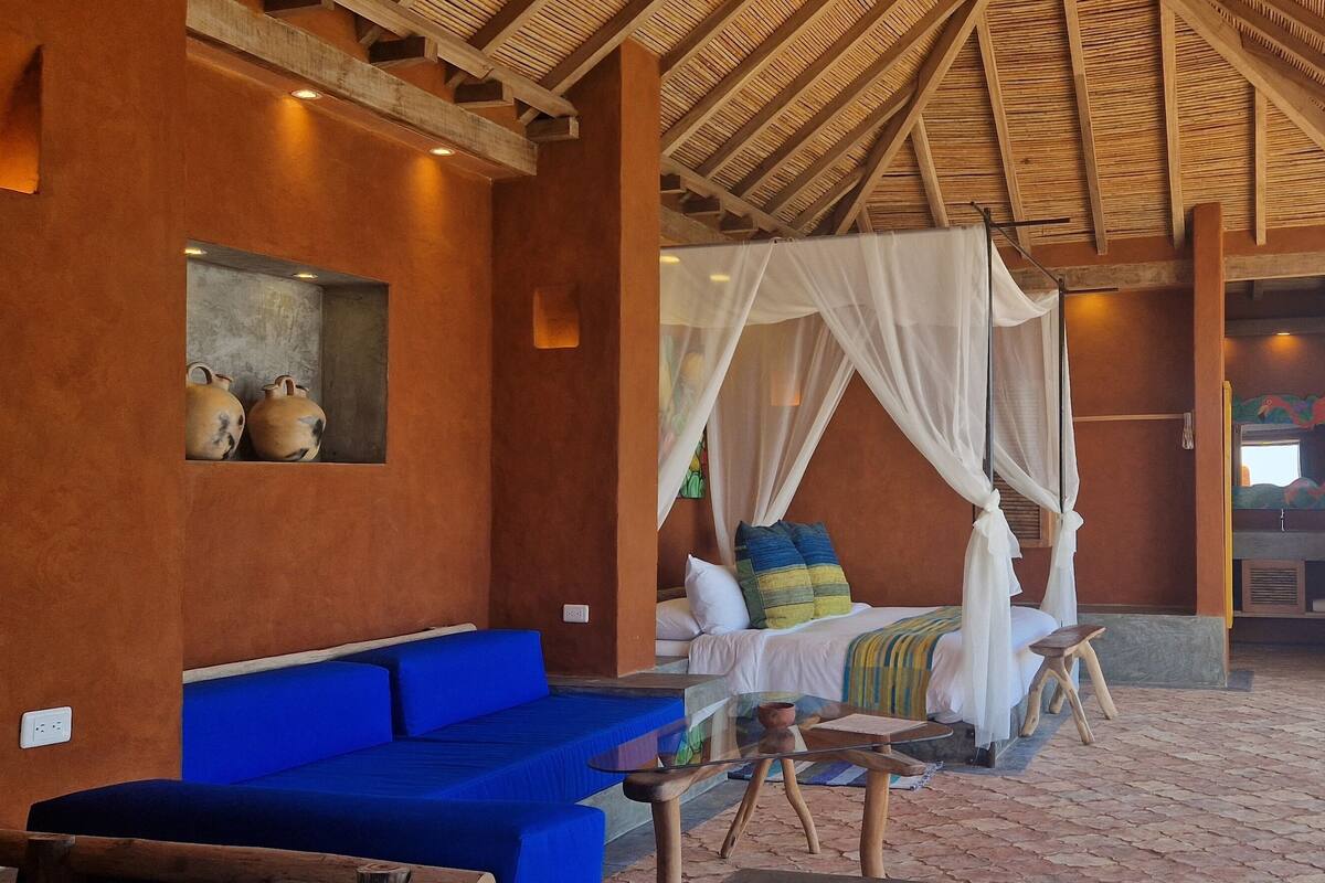 Una habitación con una cama, un sofá azul, una mesa de vidrio y vistas al mar.