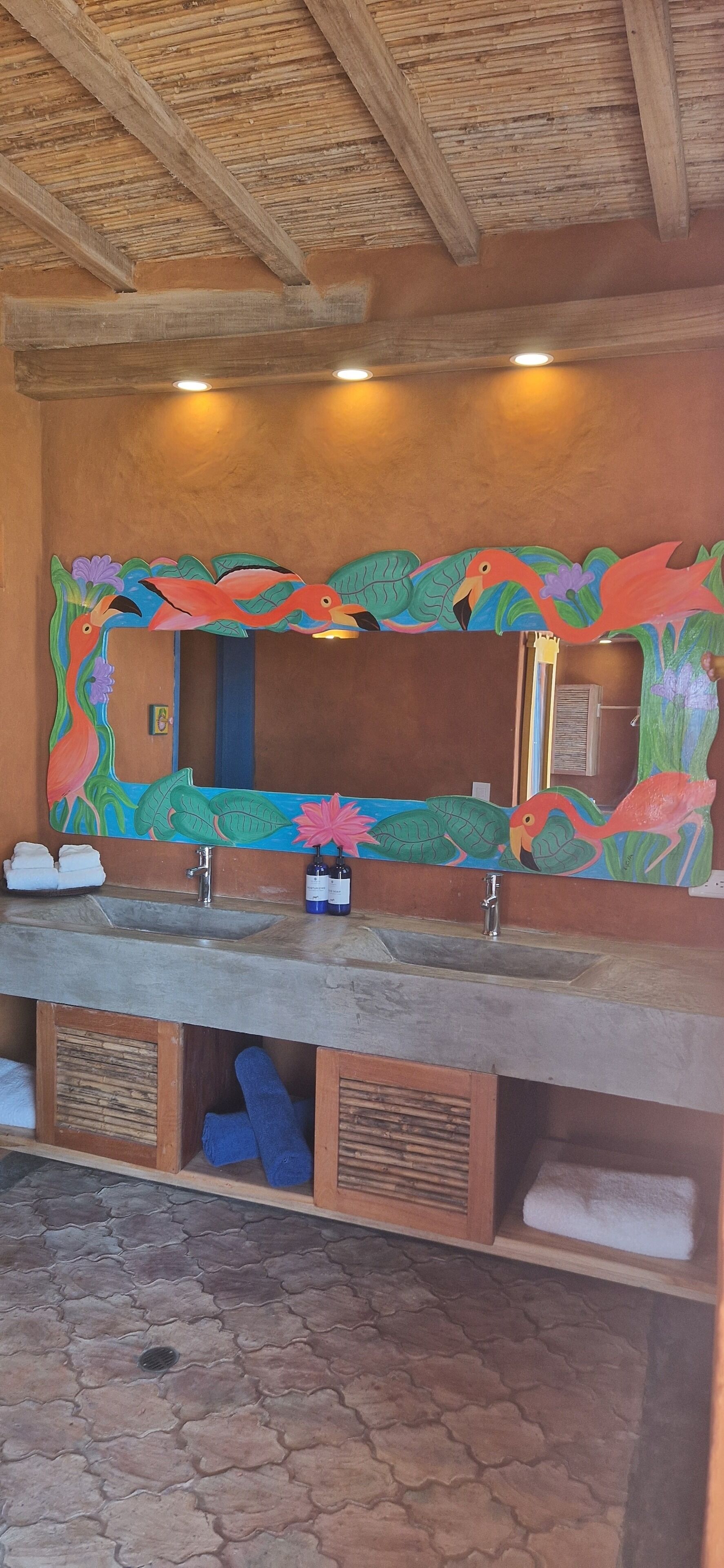 A bathroom with a large mirror, wooden ceiling, and tiled floor.