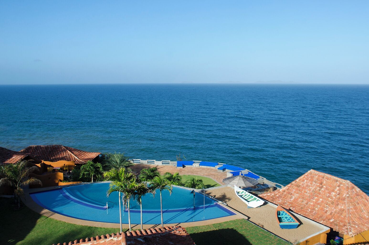 A resort with a swimming pool, palm trees, and a view of the ocean.